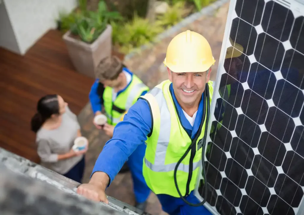 Engenheiro instalando painéis solares no telhado com equipe ao fundo, promovendo energia renovável e sustentabilidade.