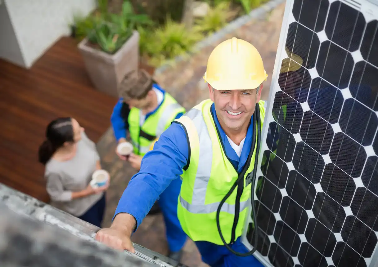 Engenheiro instalando painéis solares no telhado com equipe ao fundo, promovendo energia renovável e sustentabilidade.