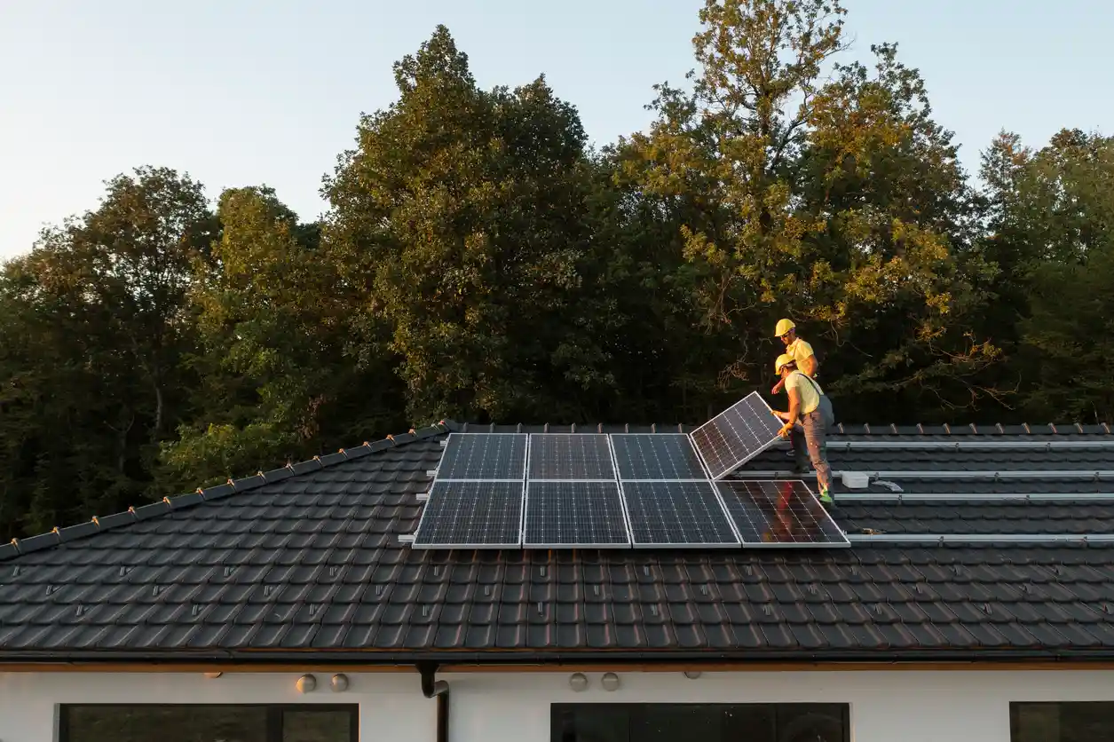 Engenheiros instalando painéis solares em telhado de residência, promovendo energia limpa e sustentável, com fundo de árvores verdes e céu claro.