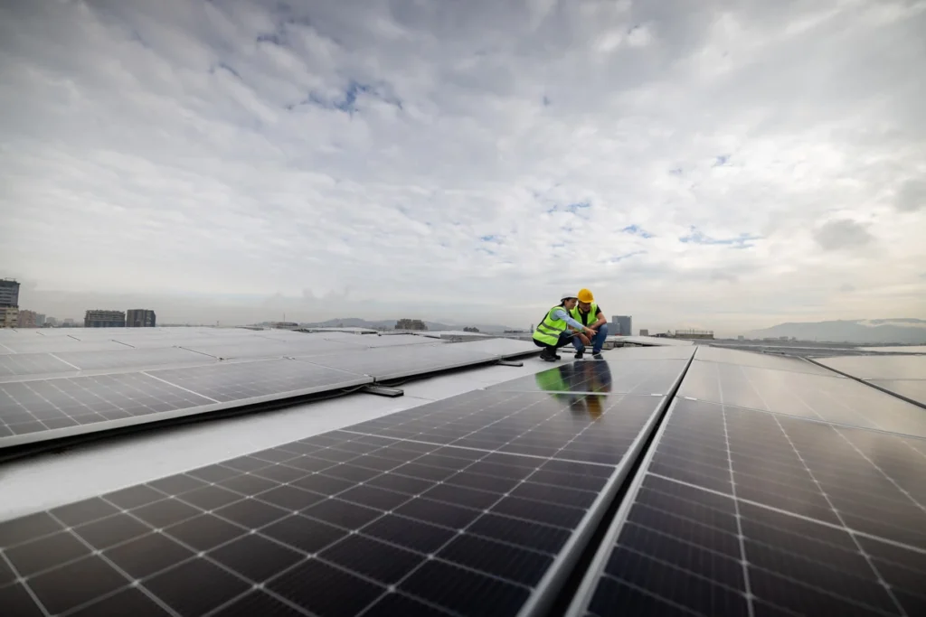 Funcionários instalando painéis solares em um telhado, símbolo de energia renovável e sustentabilidade ambiental, sob céu nublado.