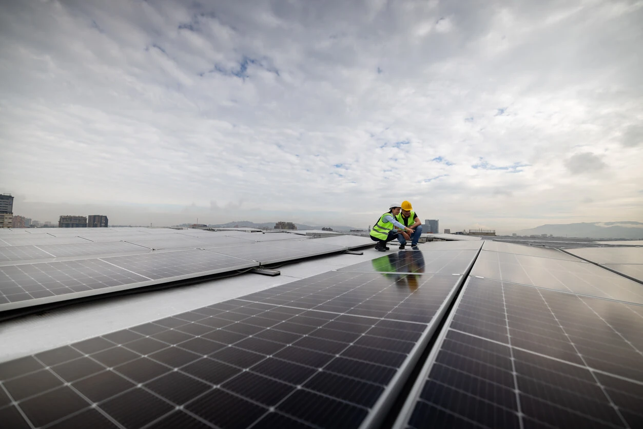 Funcionários instalando painéis solares em um telhado, símbolo de energia renovável e sustentabilidade ambiental, sob céu nublado.