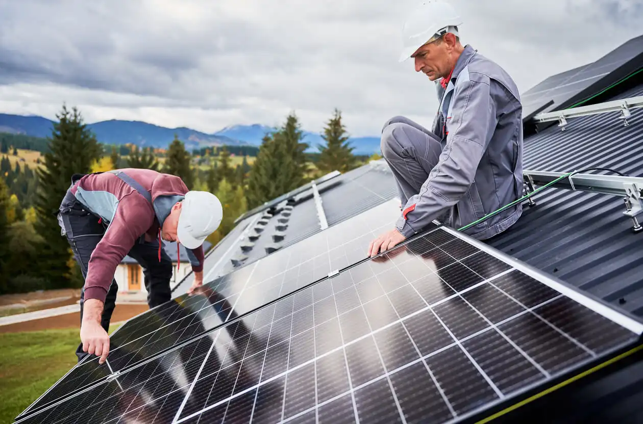 Duas pessoas instalando painéis solares em telhado com uma paisagem de natureza ao fundo, promovendo energia renovável e sustentabilidade.